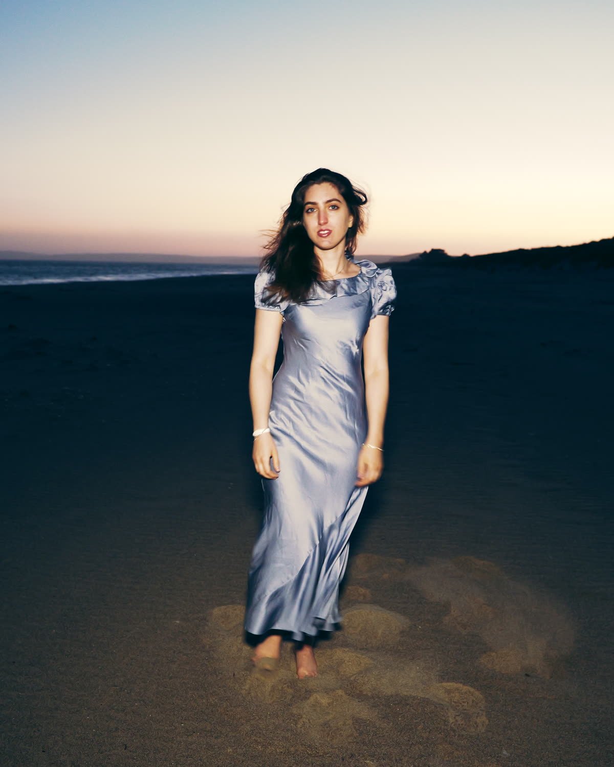 Editorial portrait on wet sand at dusk, lit against the last of the sky